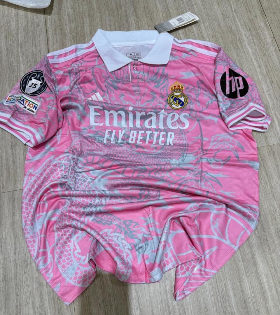 Pink Real Madrid adidas jersey with dragon pattern laid flat on wooden floor.