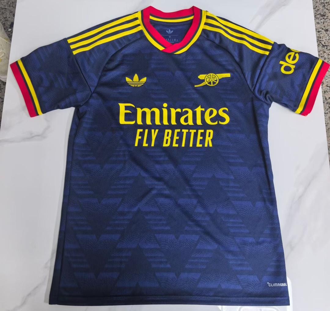 Navy blue Arsenal football jersey with yellow accents and sponsor logos laid flat.