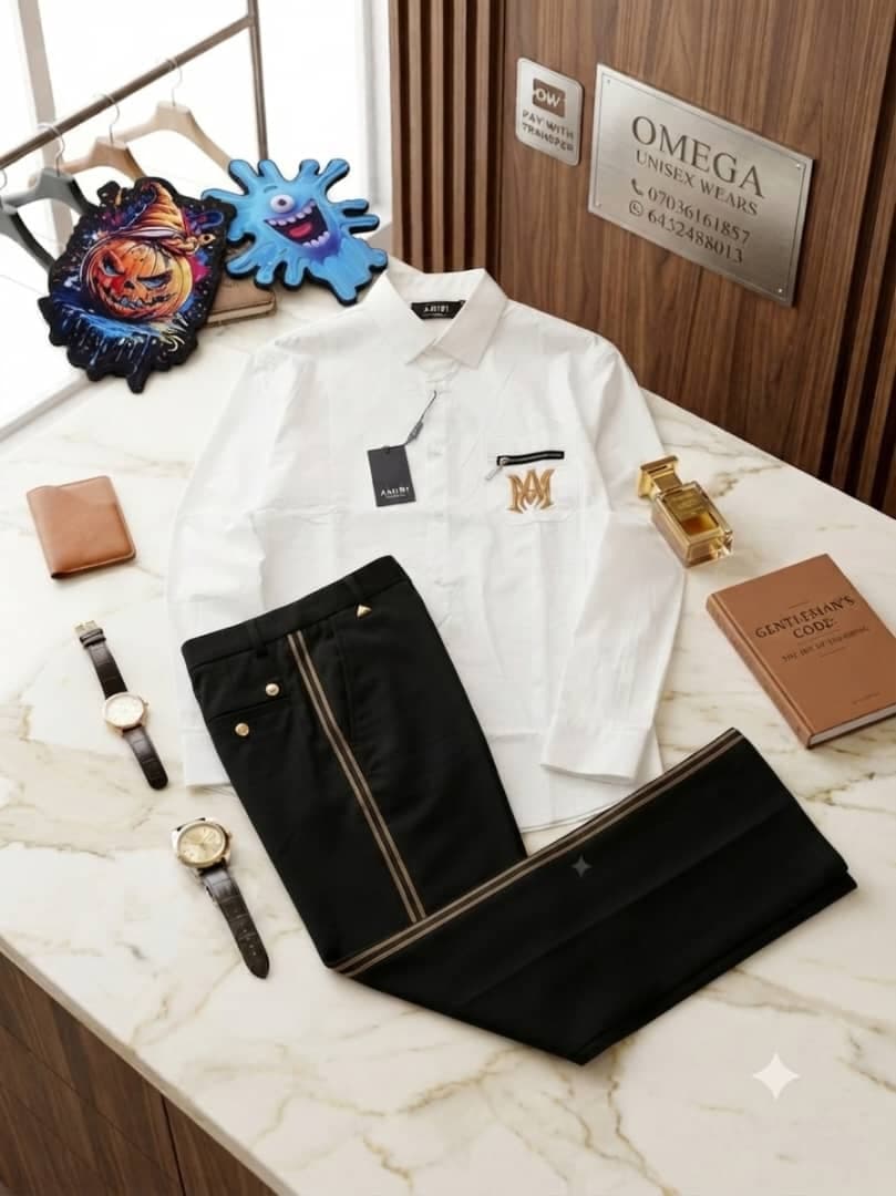 White Amiri shirt with MM logo and black side-striped trousers on marble countertop with fashion accessories.