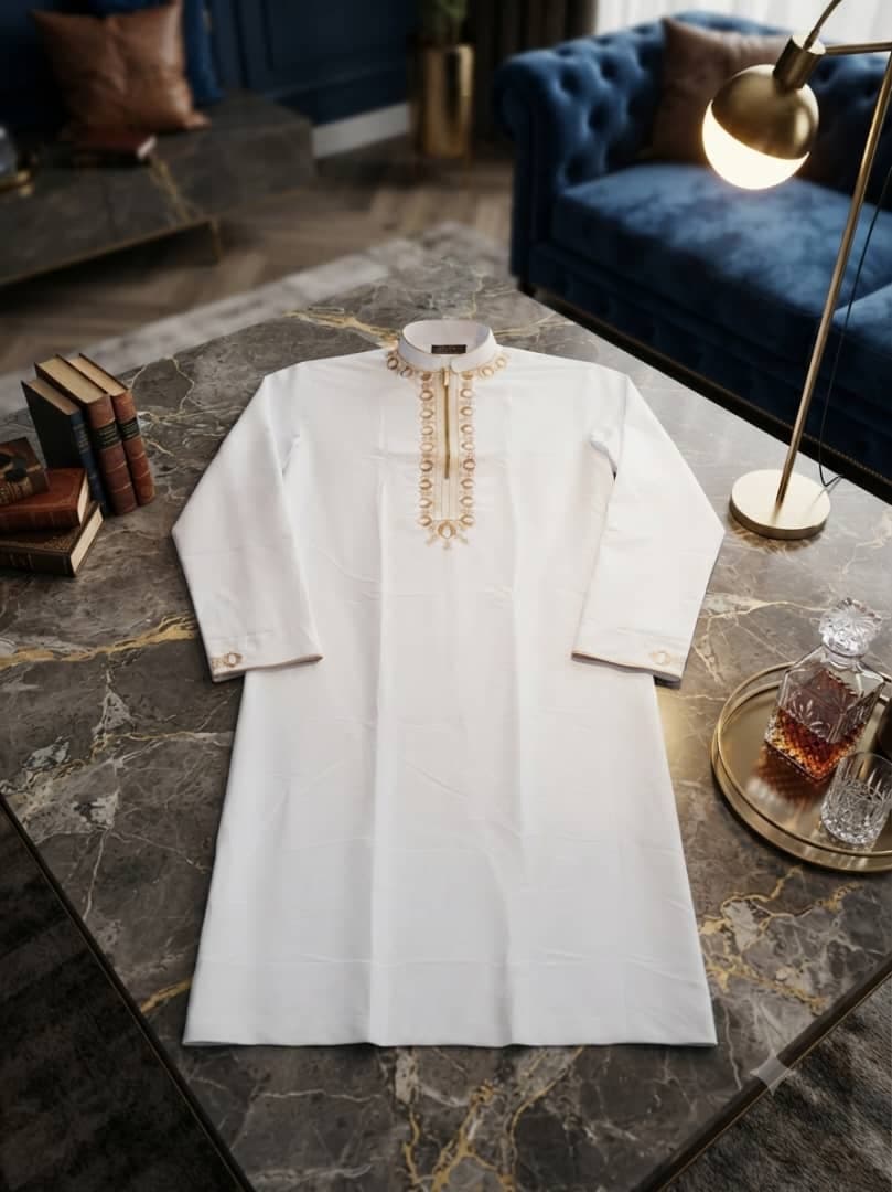 White long sleeve jalabia with gold embroidery on marble table.