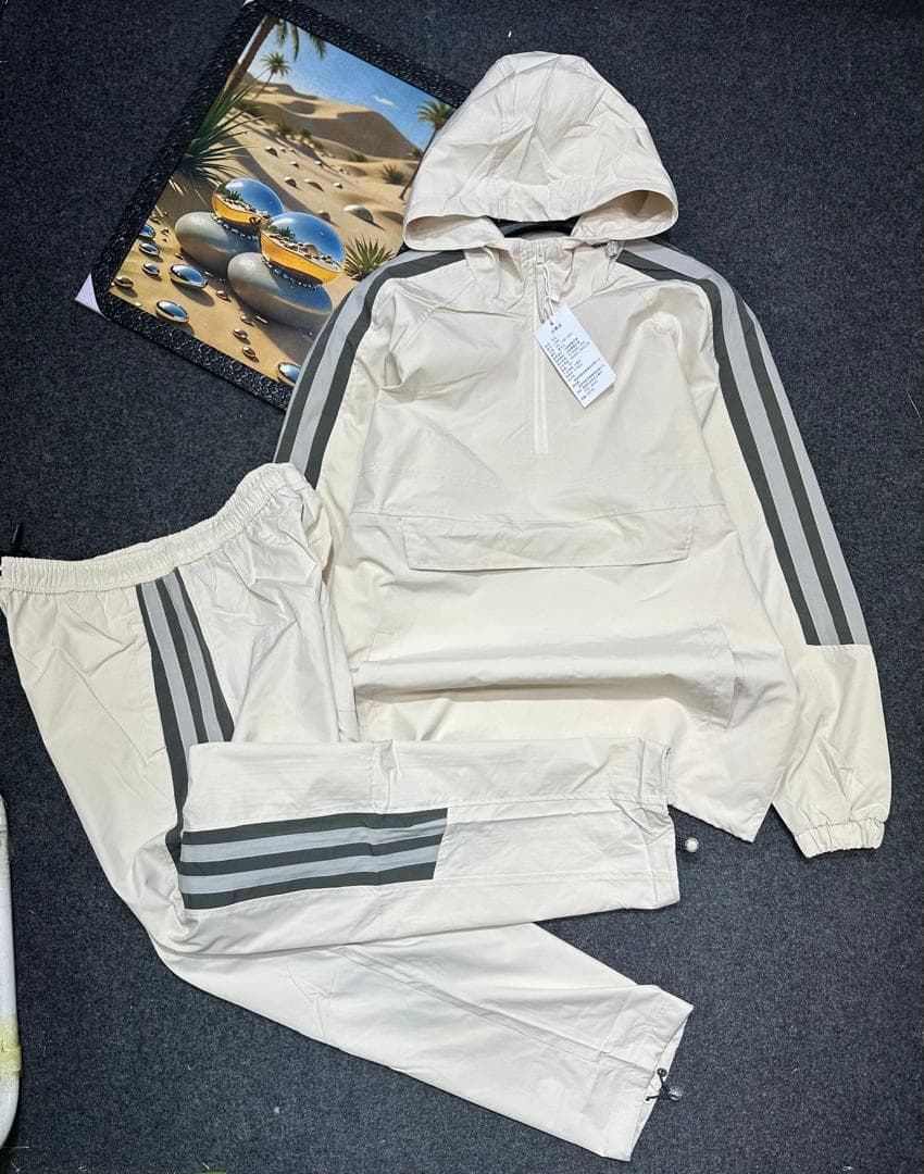 Cream hooded cargo tracksuit laid flat showing quarter-zip top and striped pants.