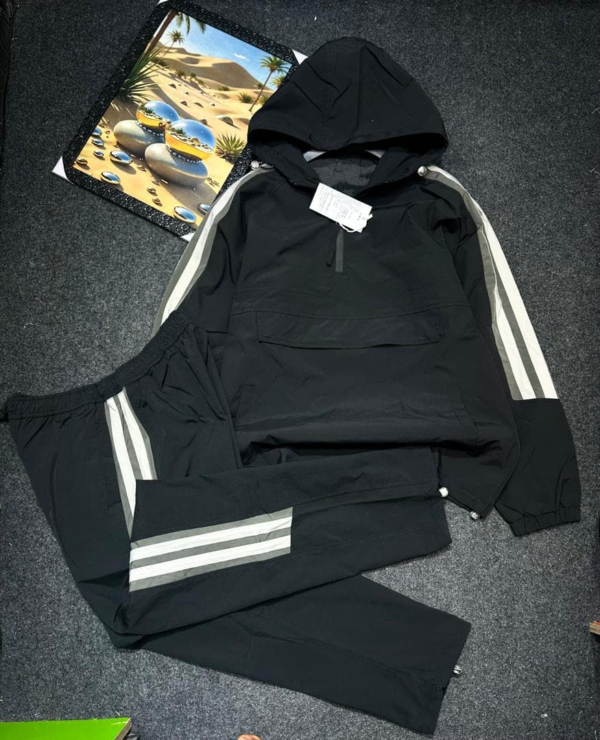 Black hooded cargo tracksuit laid flat showing quarter-zip top and striped pants.