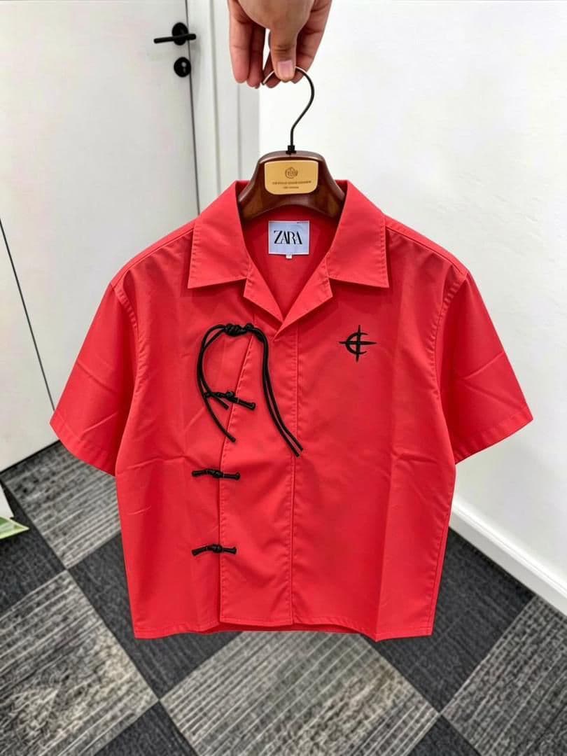 Red short sleeve shirt with frog buttons, drawstring and chest embroidery on wooden hanger.