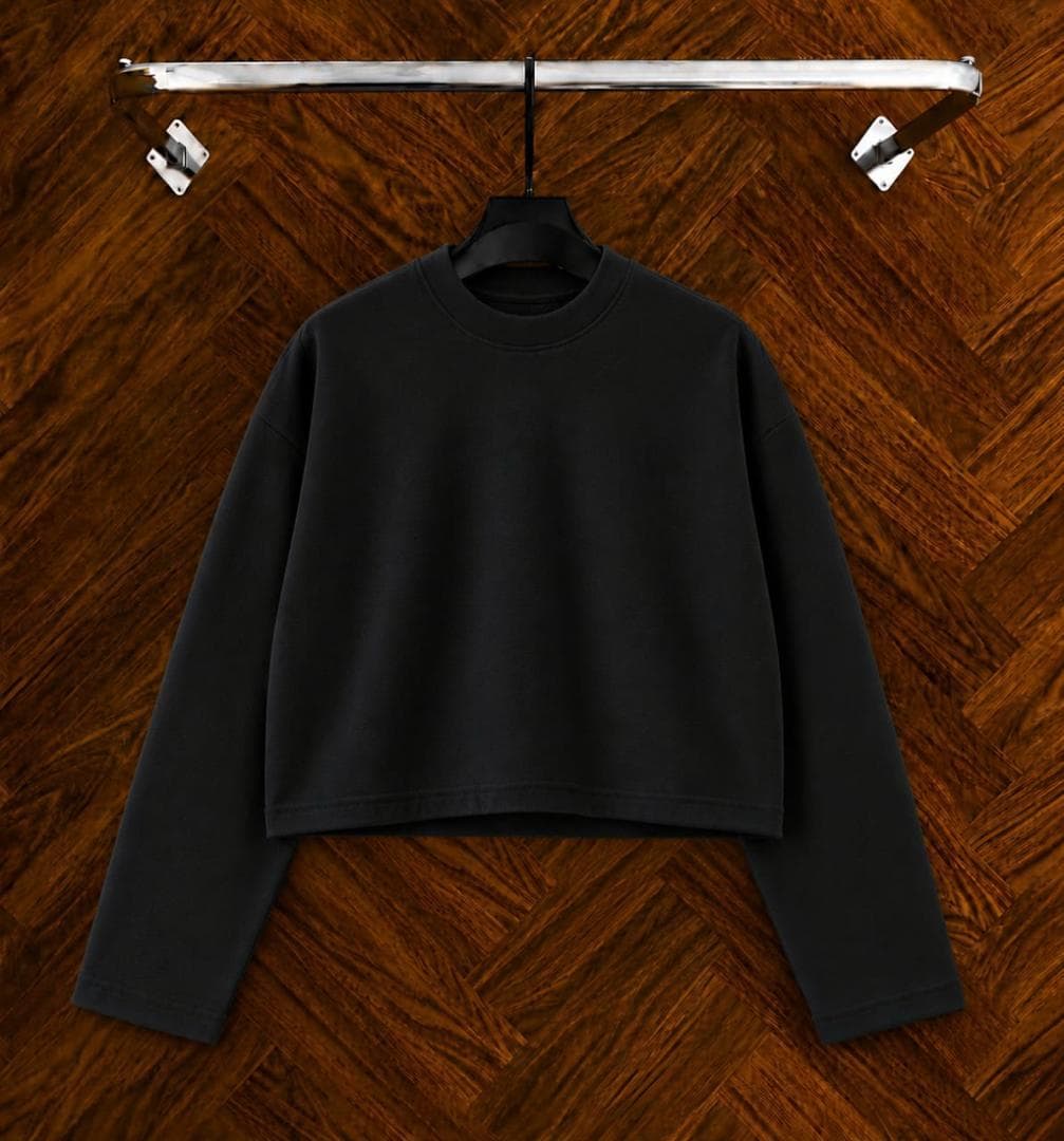 Black cropped long sleeve sweatshirt on hanger against wooden background.