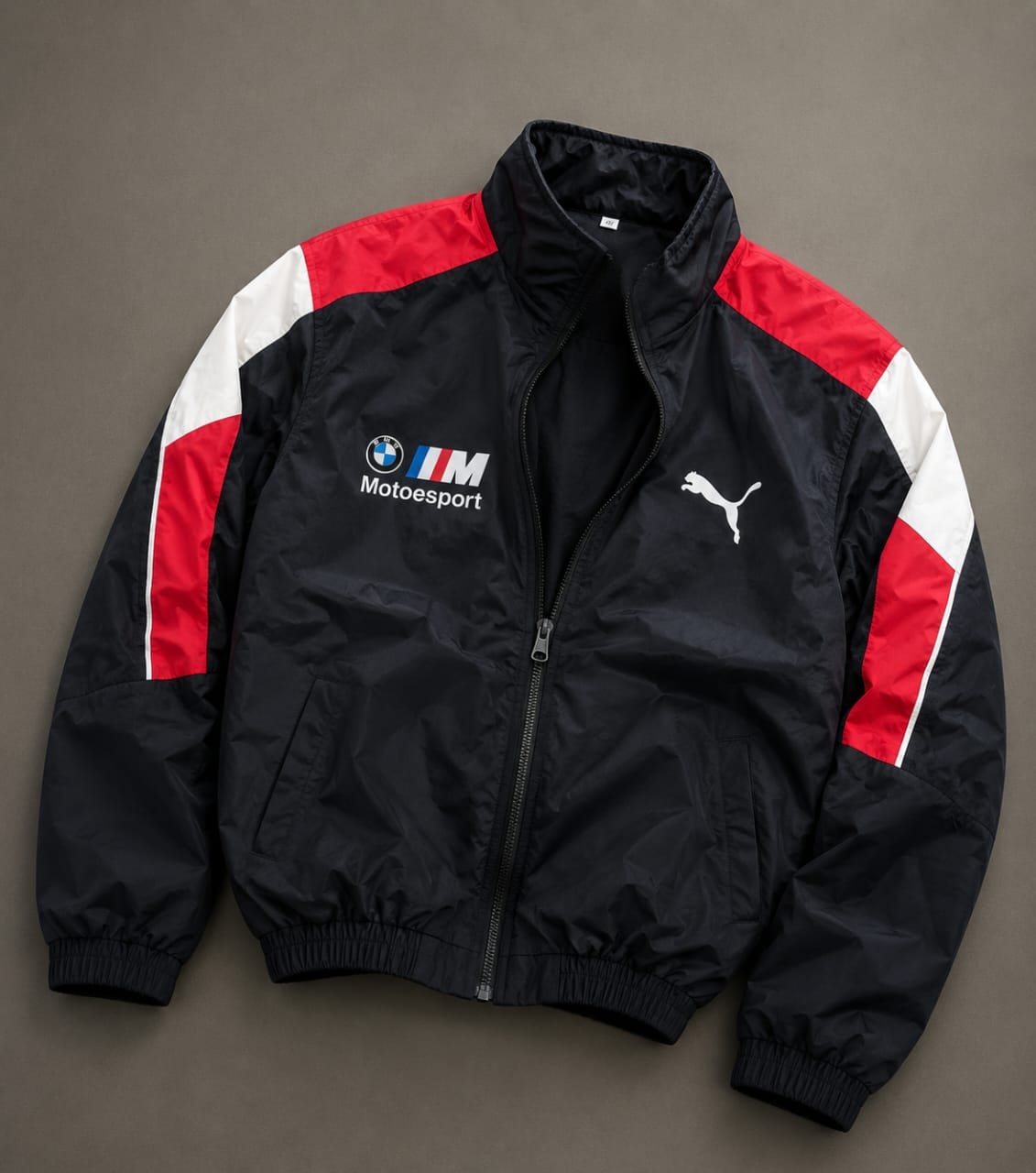 Black Puma BMW M Motorsport track jacket with red and white accents on shoulders and sleeves.