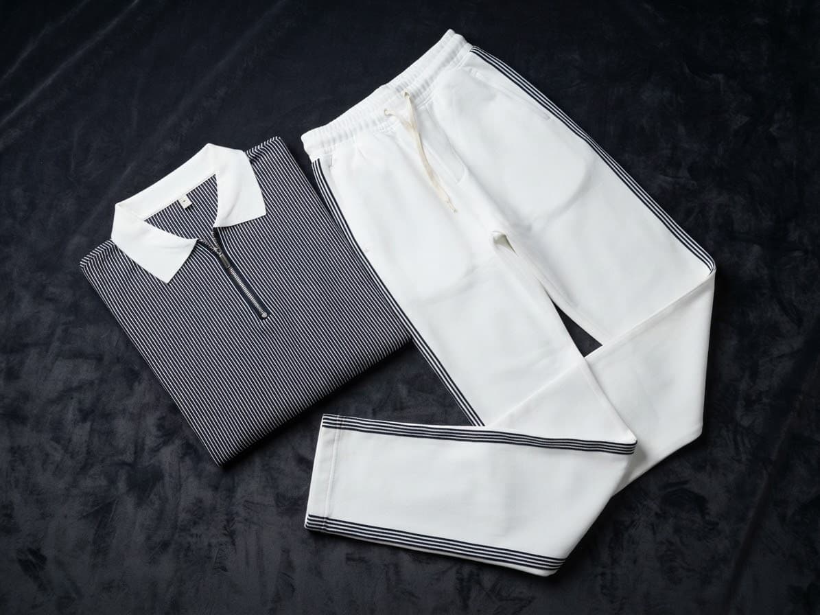 Navy pinstriped polo shirt with white collar next to white track pants with navy stripes.