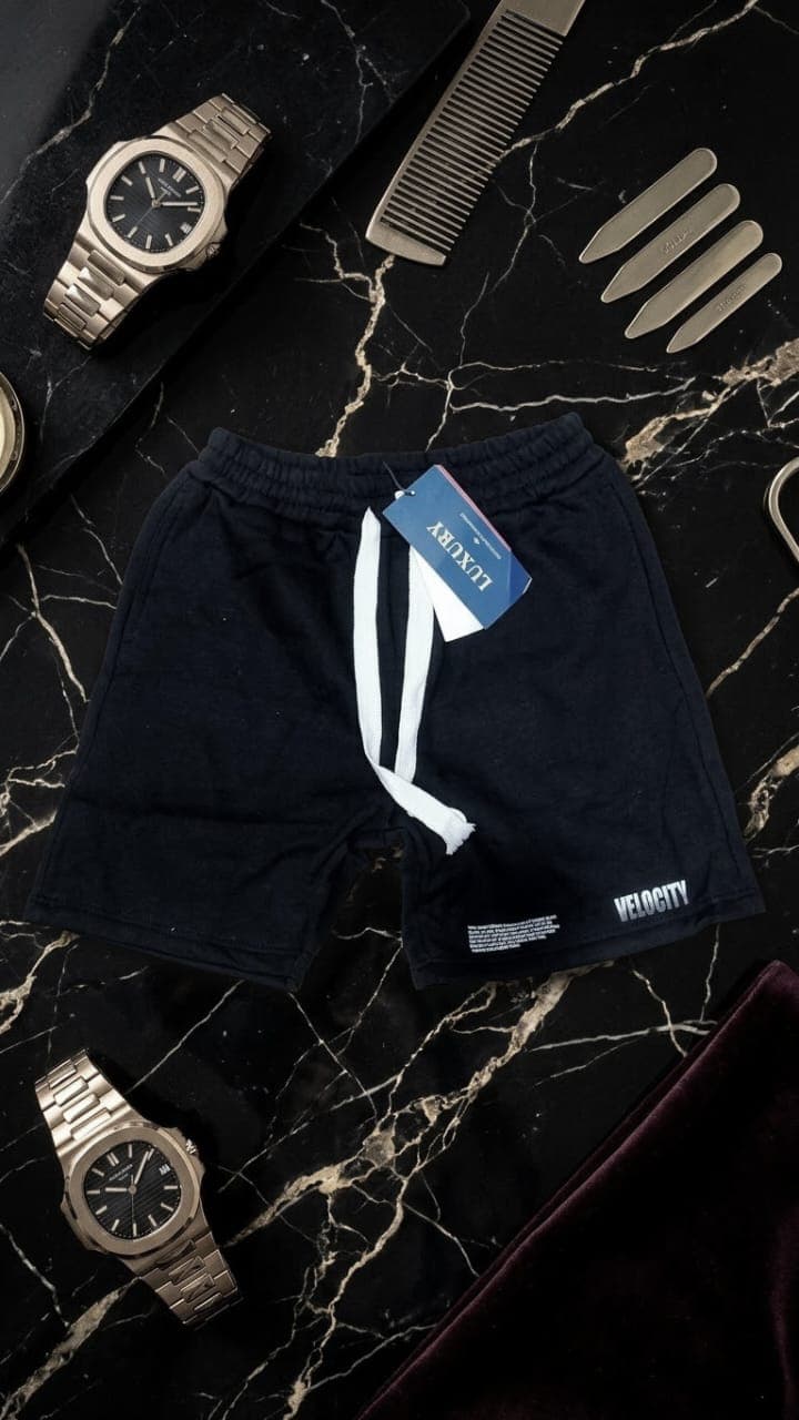 Navy fleece shorts with VELOCITY print on the leg arranged with watch and grooming items.