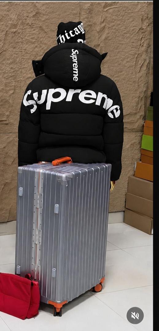 Person wearing black Supreme puffer jacket from the back showing large logo.