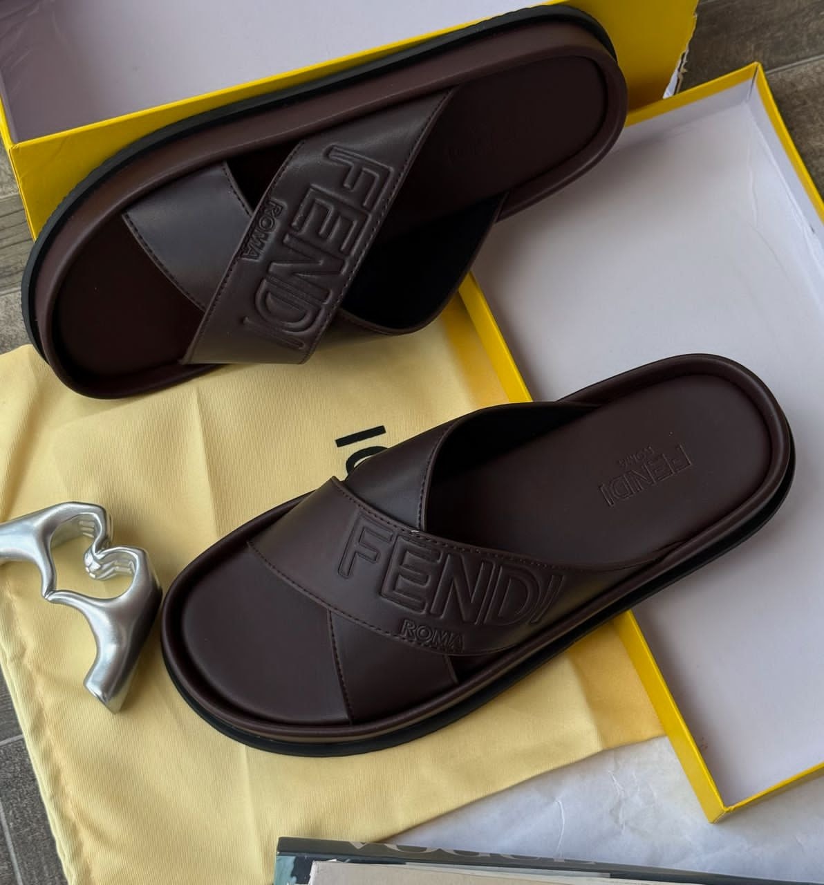 Brown Fendi slides with logo shown inside yellow box with dust bag and accessories.