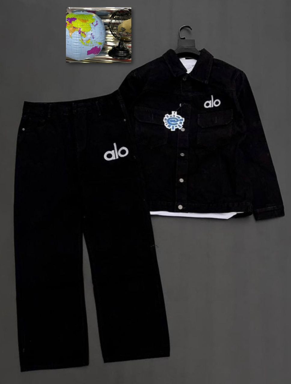 Black denim jacket with Alo text, circular chest patch and white t-shirt layered, next to black jeans with Alo logo on leg.