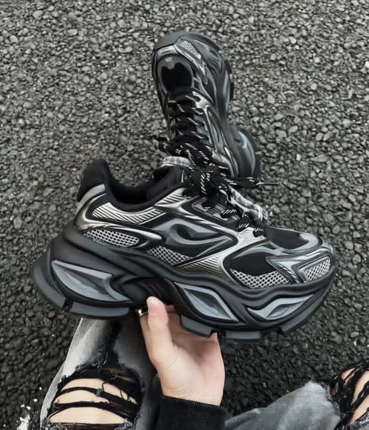 Black and silver chunky wave runner sneakers held outdoors showing detailed upper and sole.