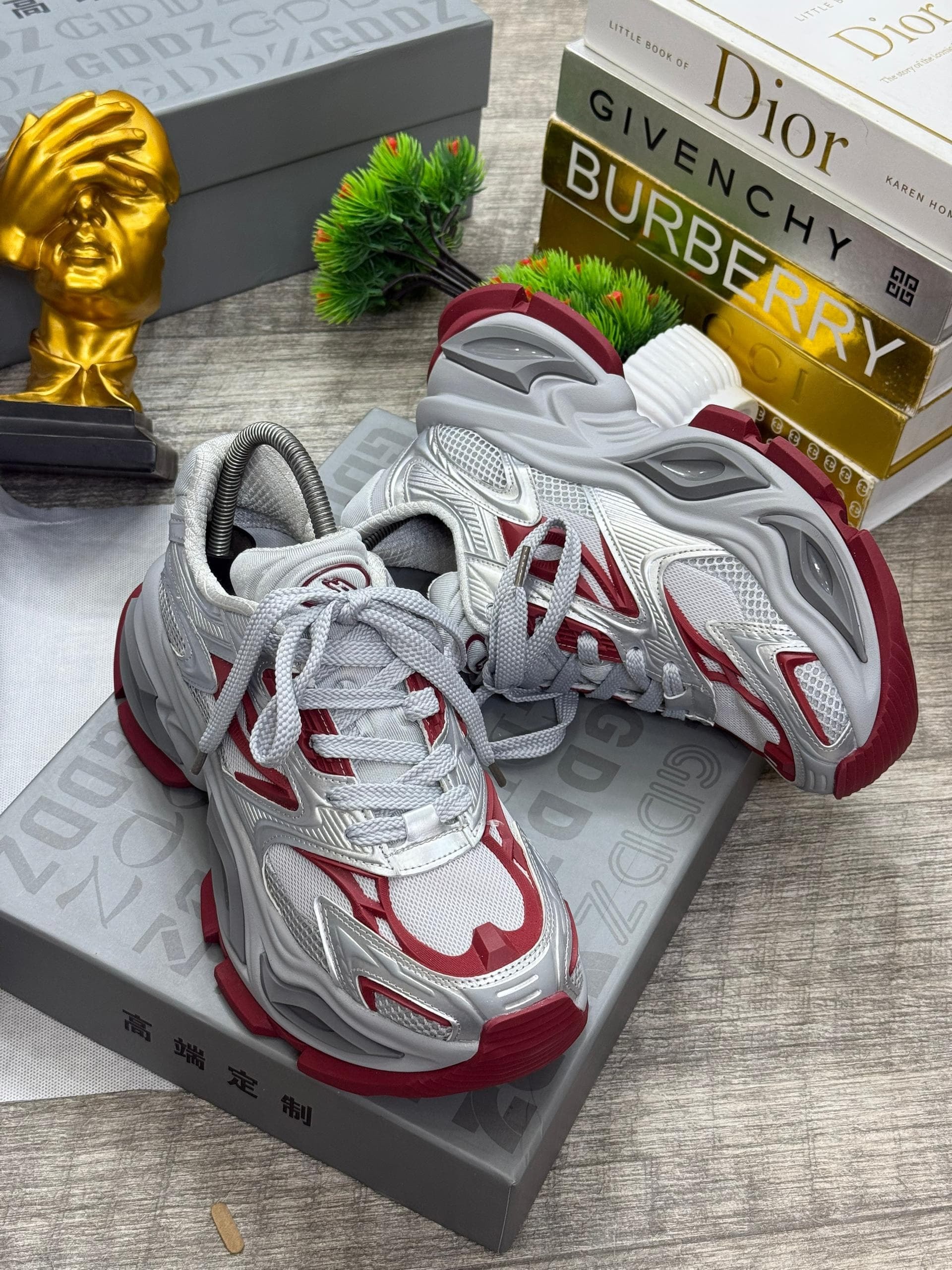 White, gray and red chunky wave runner sneakers displayed with fashion books and boxes.
