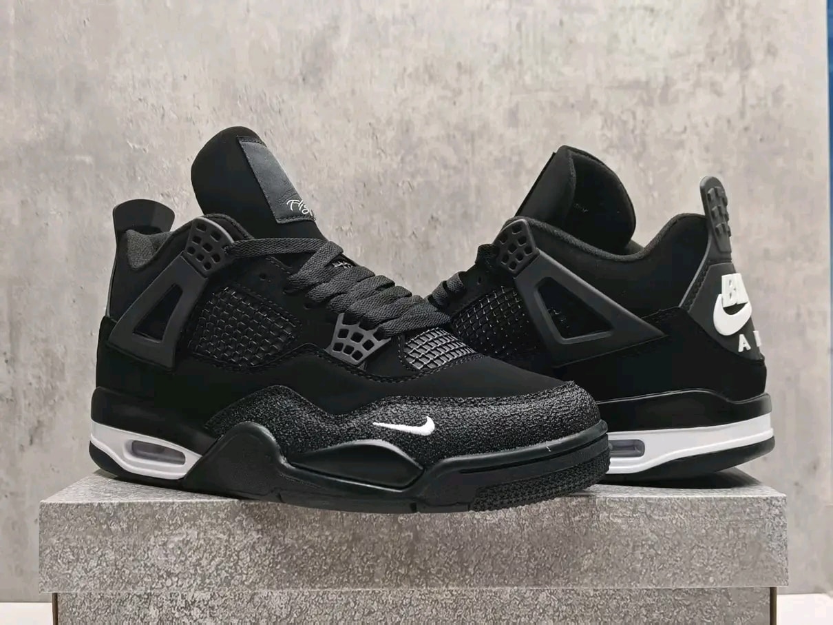 Pair of black Air Jordan 4 sneakers displayed on stone pedestal against neutral wall.