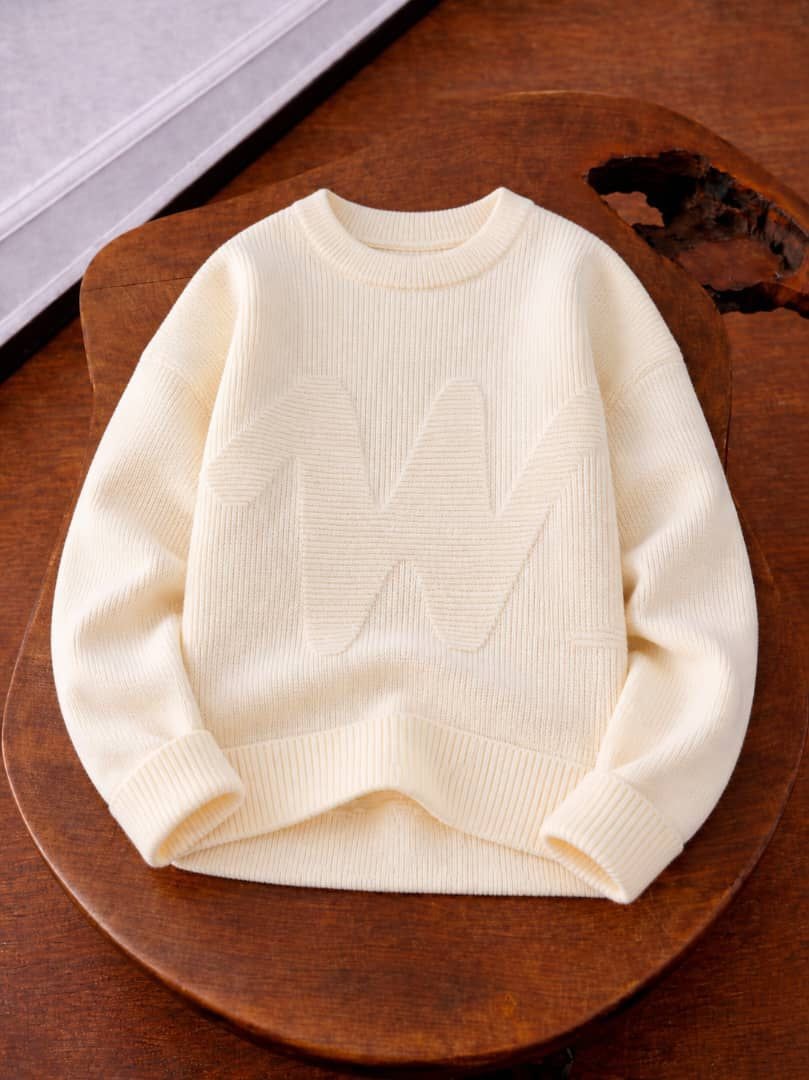 Cream knit sweater with large raised embossed pattern on chest.