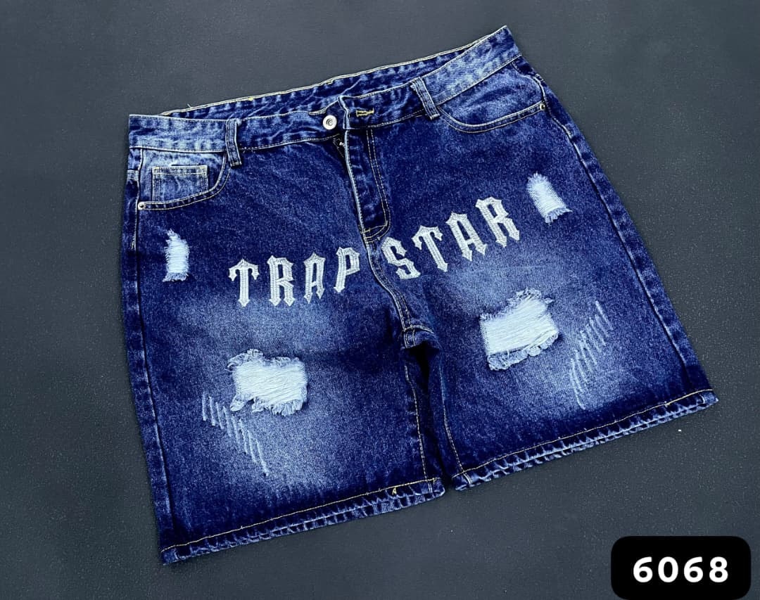 Blue denim shorts with white TRAP STAR gothic text and distressed rips.