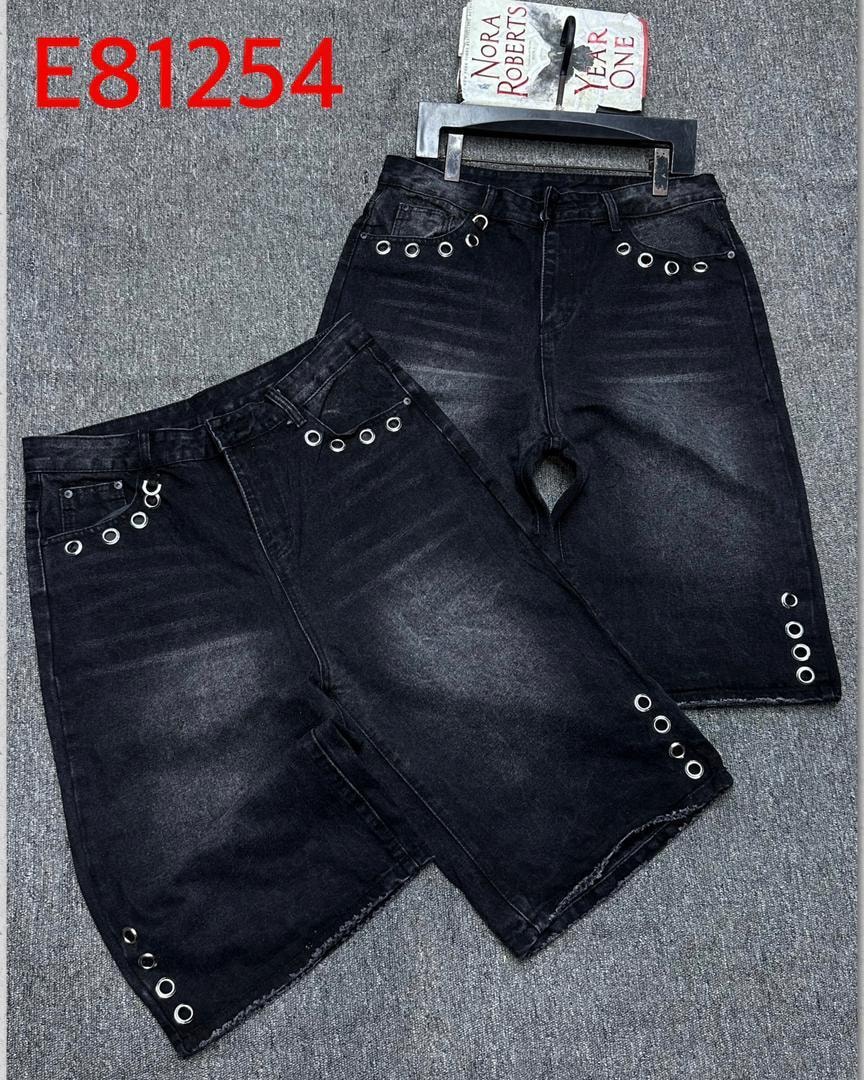 Flat lay view of black denim 3/4 shorts with multiple silver eyelets on pockets and seams.