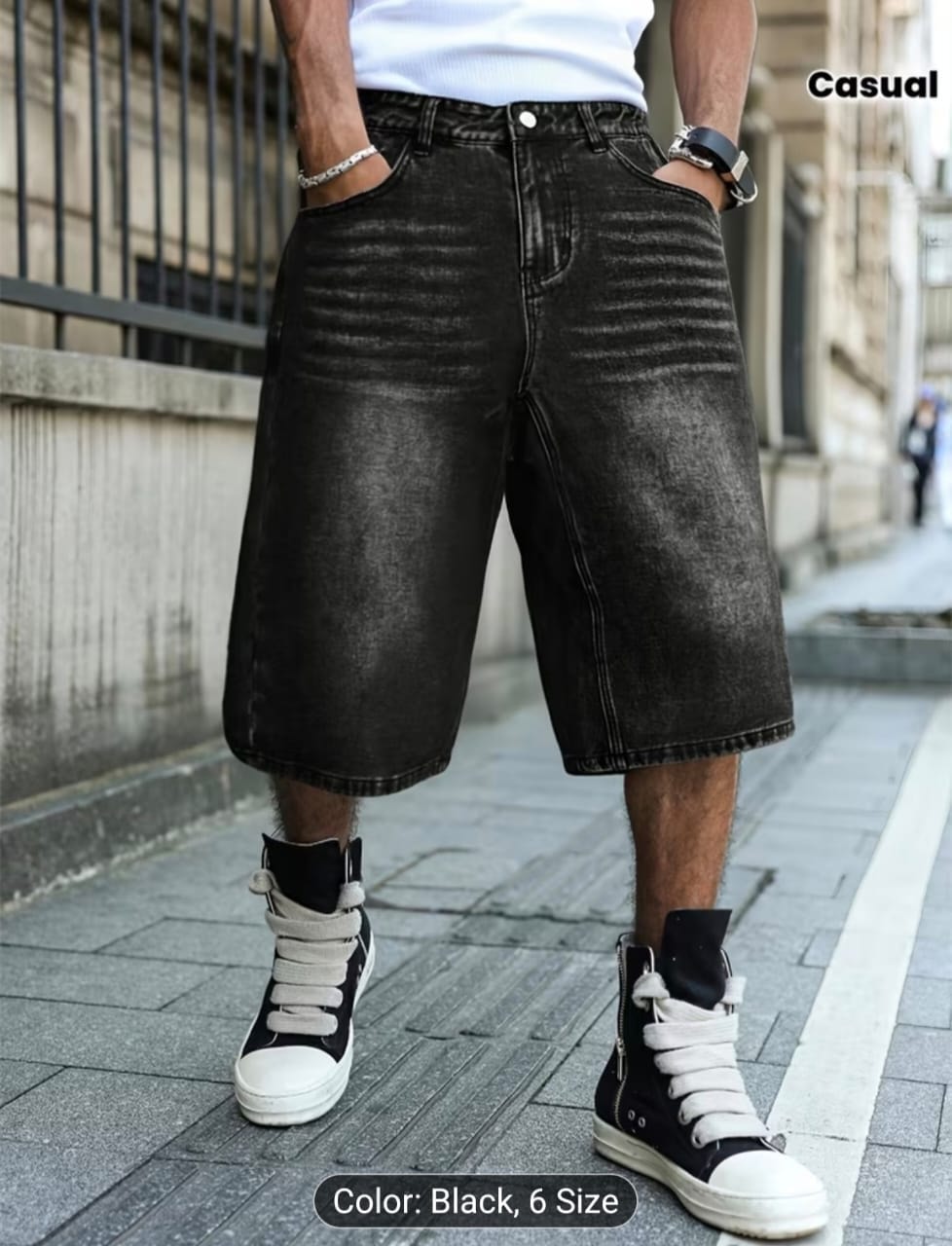 Man modeling black 3/4 jean shorts with hands in pockets, paired with white top and high-top sneakers.