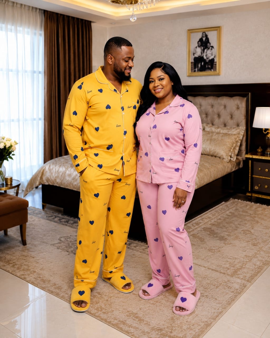Couple wearing yellow and pink heart pattern pajamas posing in a bedroom.