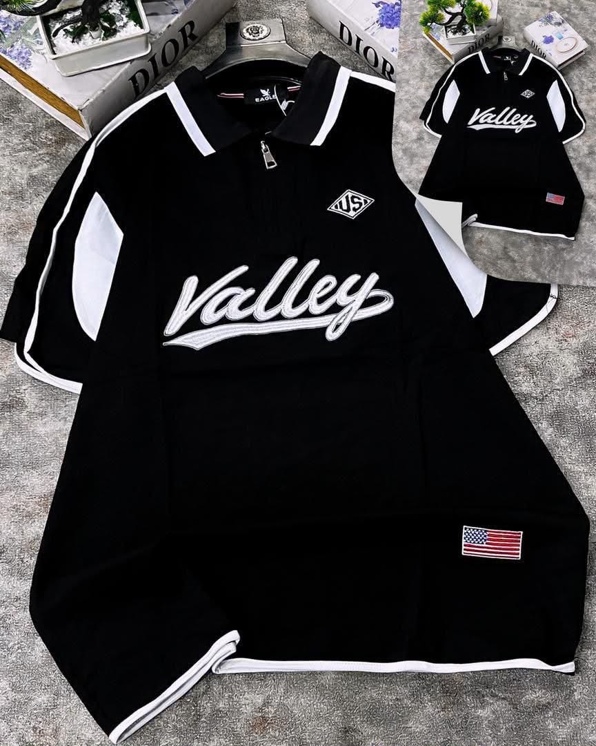 Black Valley script polo shirt with white contrast panels, embroidered logo, and American flag patch on sleeve.