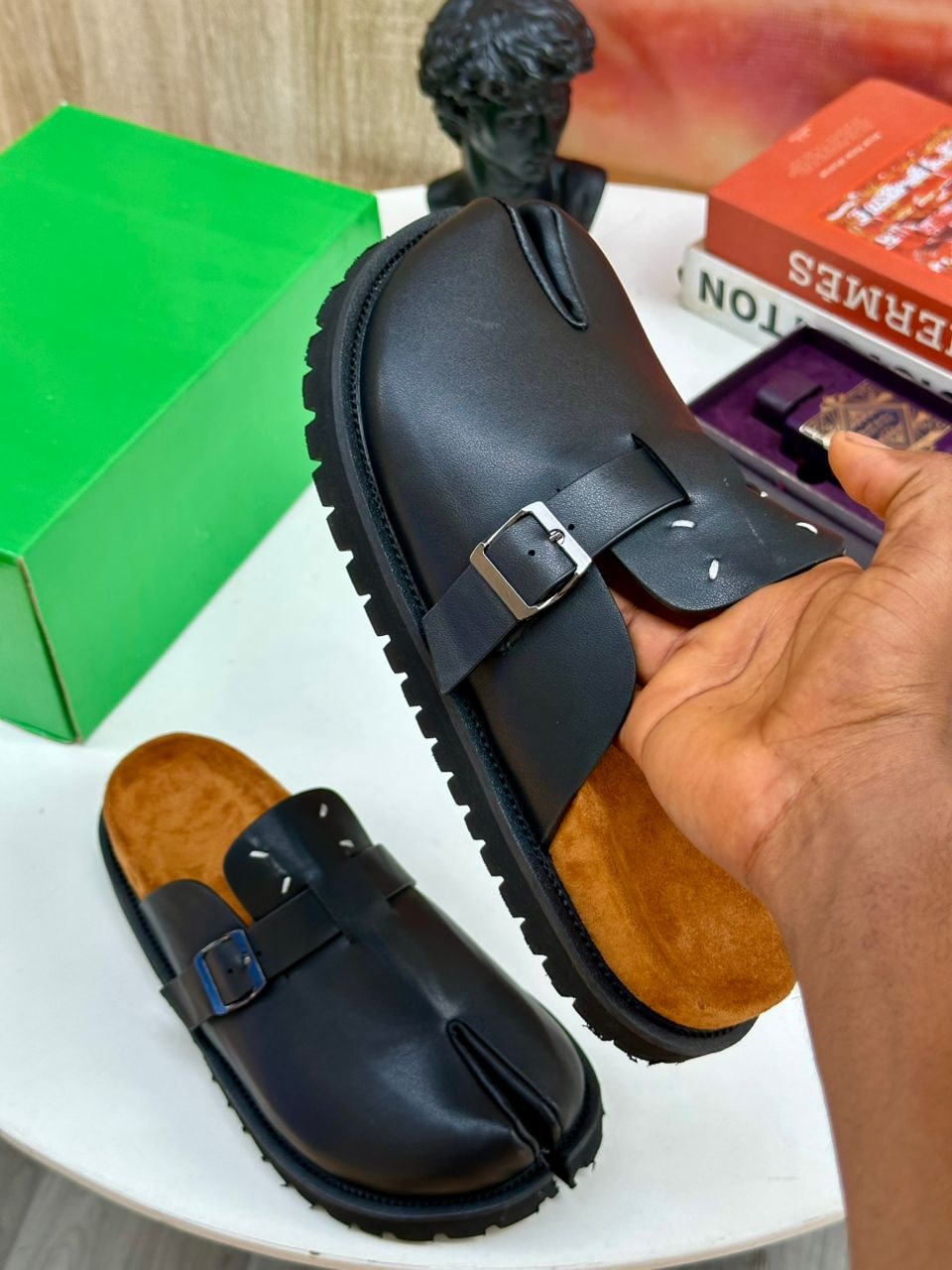 Black leather buckle mules held by hand showing interior and sole detail.