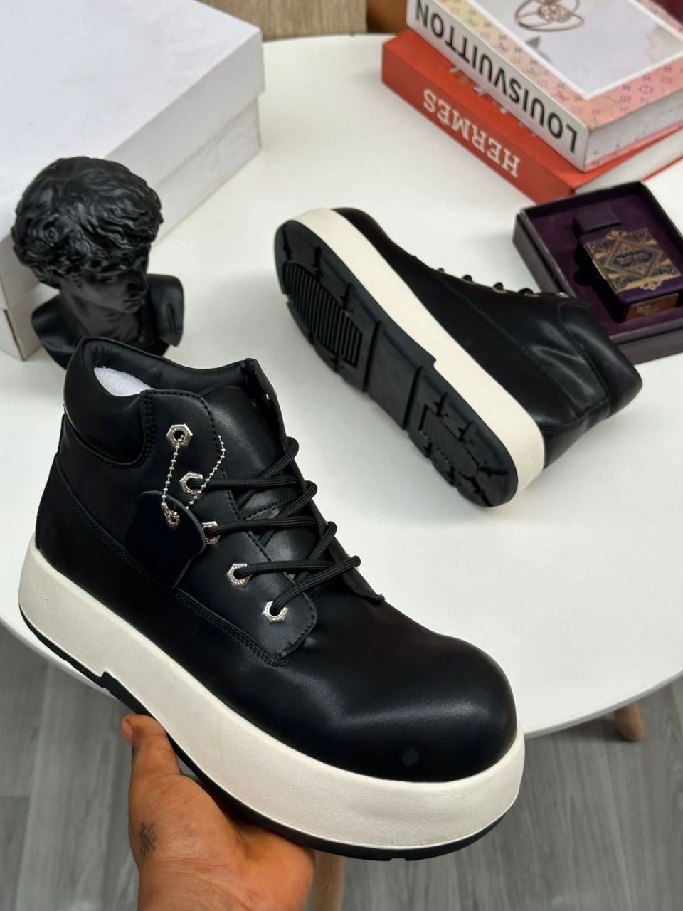 Black platform ankle boots with chain accents and thick white sole held by hand.