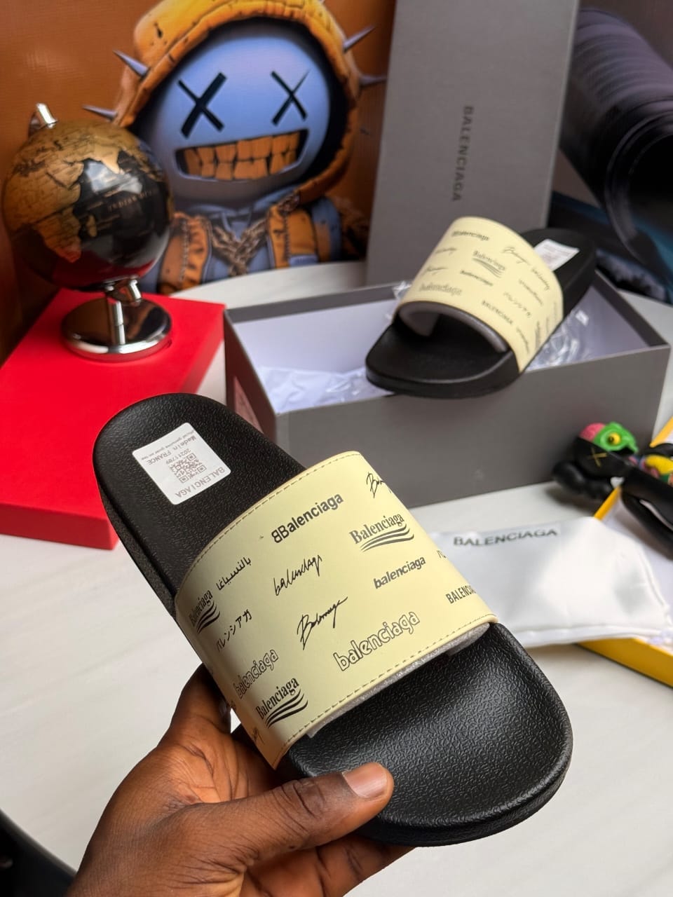 Beige Balenciaga slides with repeating logo print on strap.