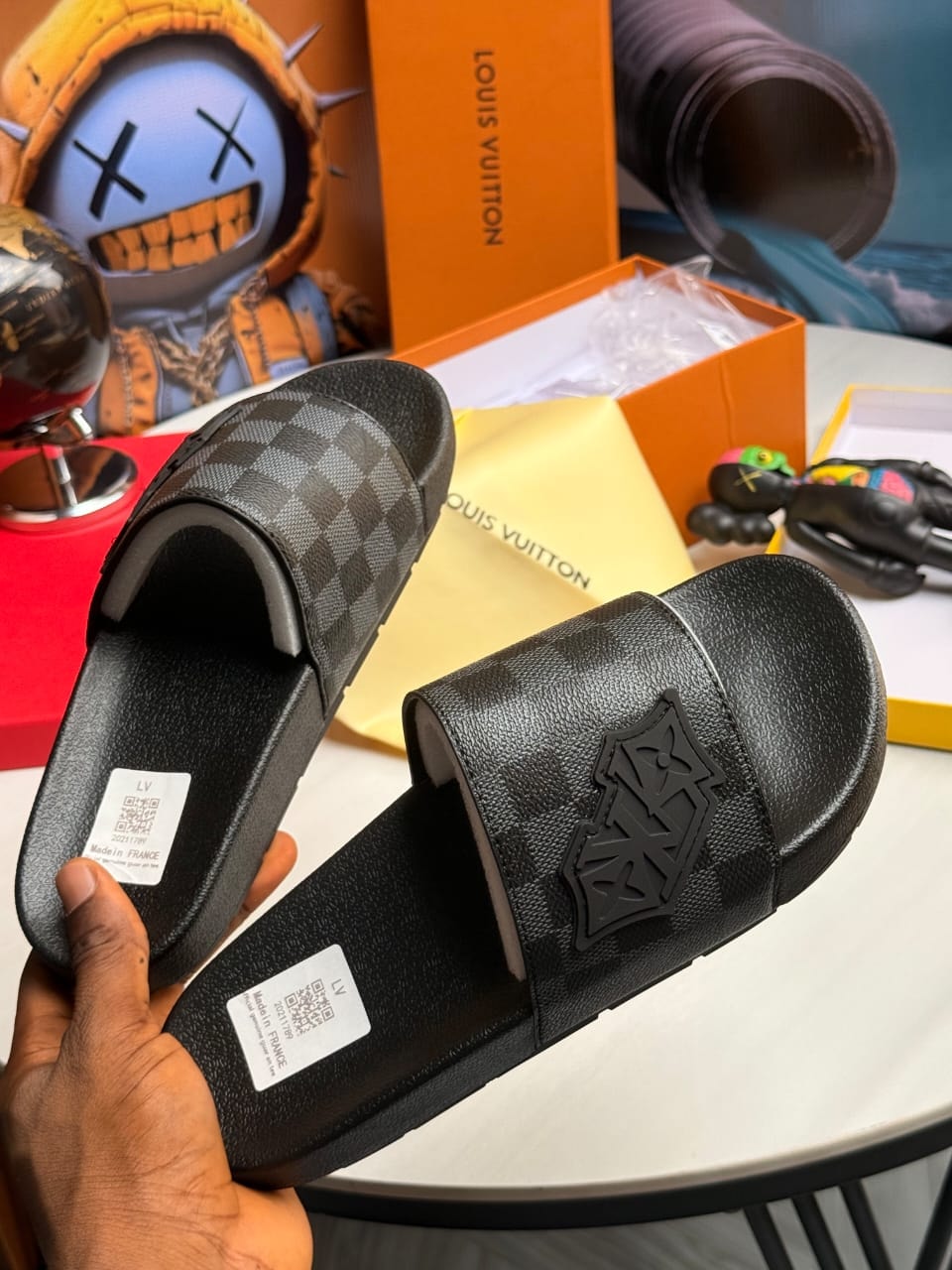 Louis Vuitton black damier pattern slides with LV emblem.