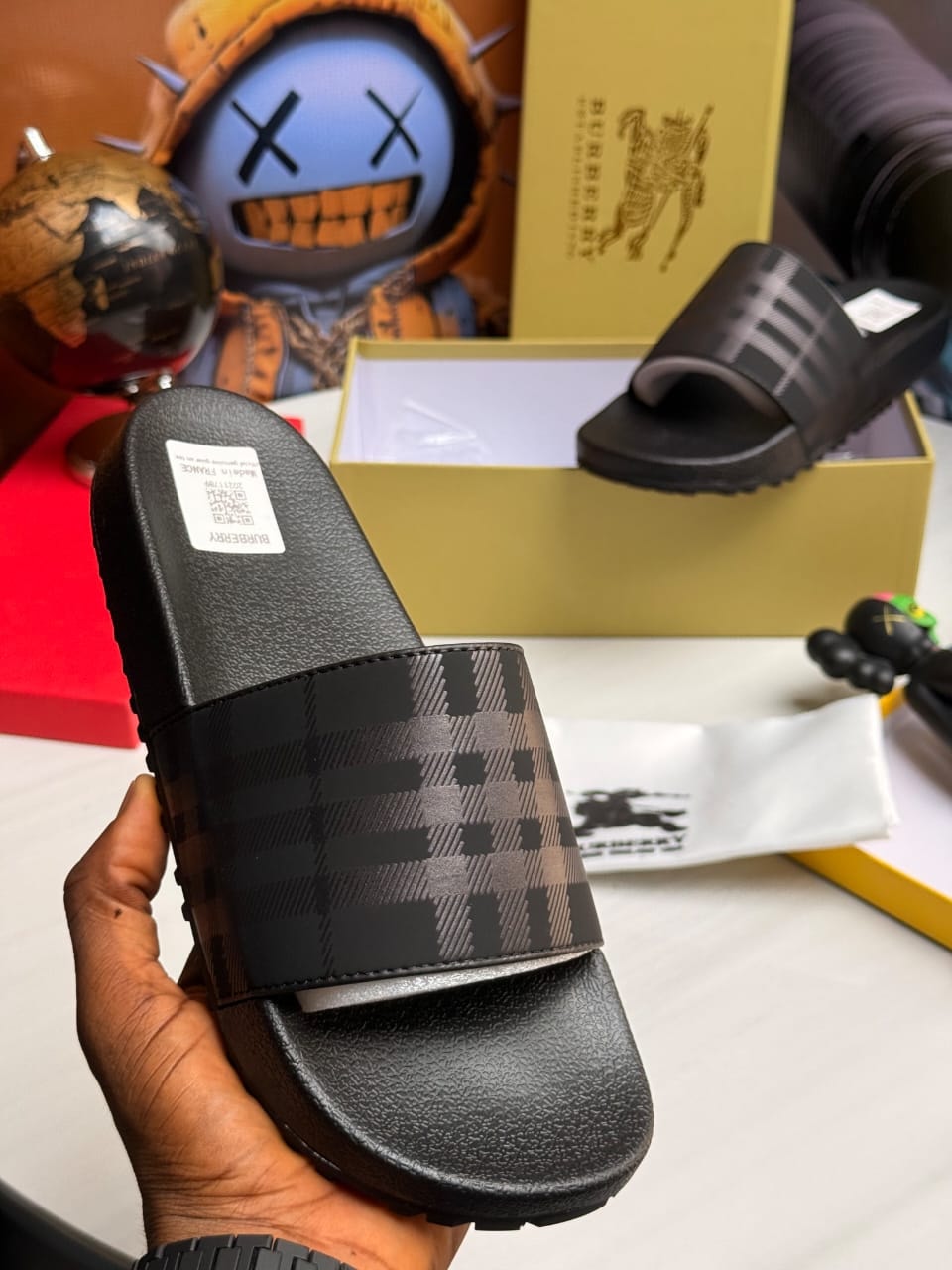 Black and grey Burberry checkered slides with logo details.