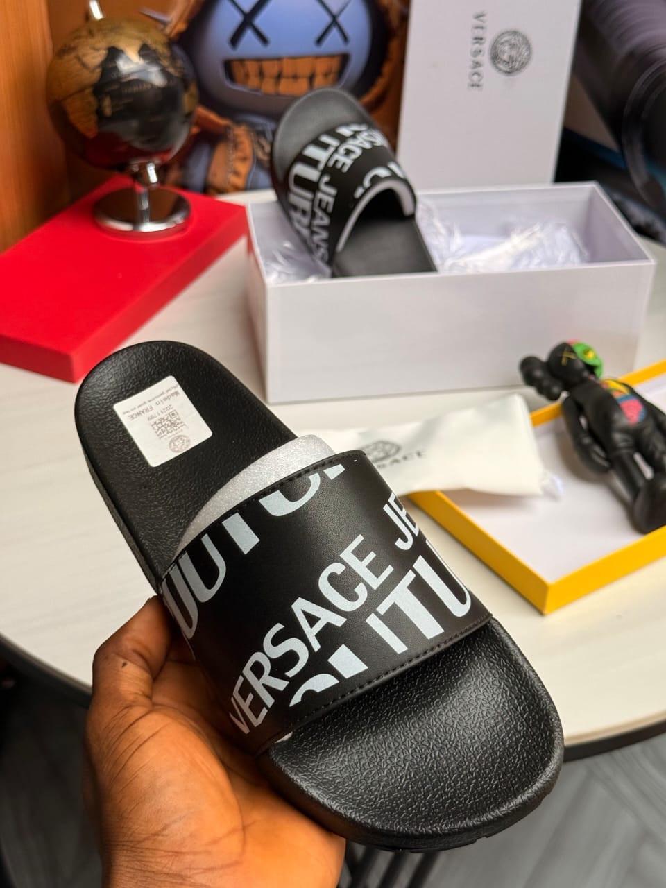 Black Versace Jeans slide held in hand with prominent text branding.