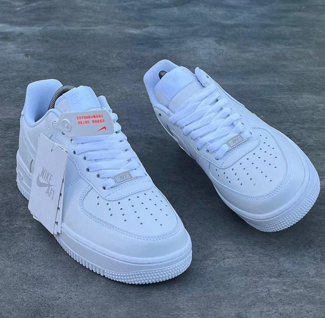 White Nike Air Force 1 sneakers on gray surface with tags attached.