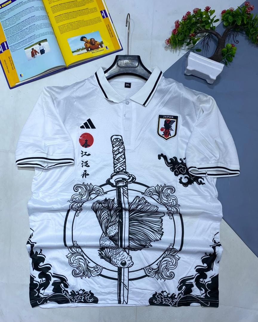 White Japan soccer jersey with large koi fish, sword graphic, and crest laid on surface.