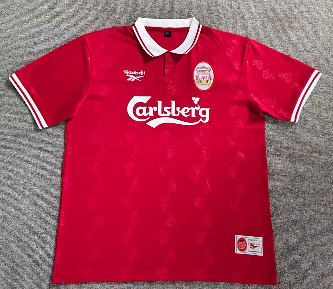 Red Liverpool soccer jersey with Carlsberg sponsor laid flat on gray background.