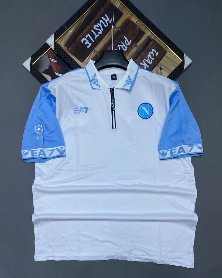 White and blue EA7 Napoli soccer jersey on hanger with logos and crest.