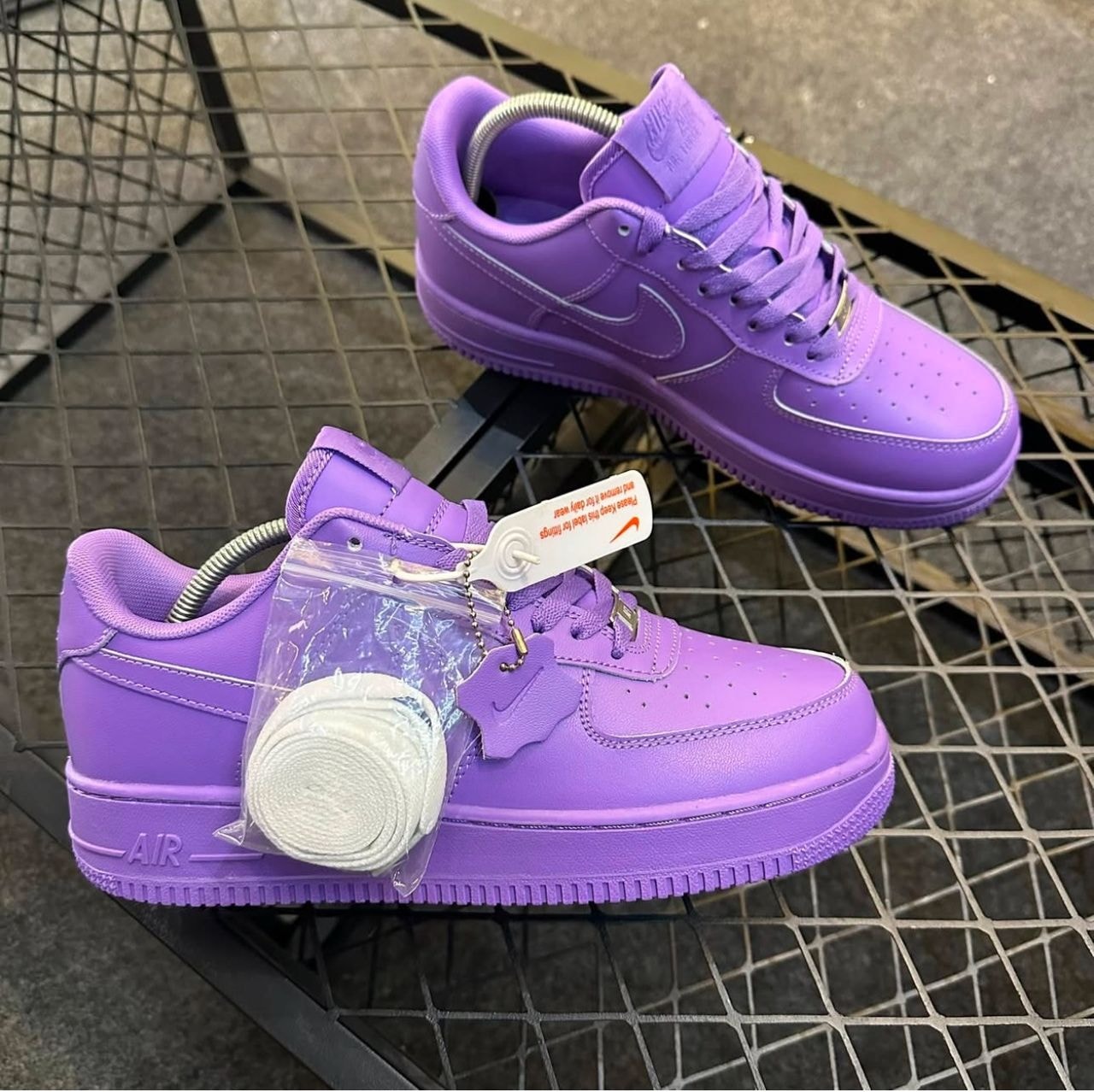 Purple Nike Air Force 1 sneakers on metal grid with extra laces and tags.