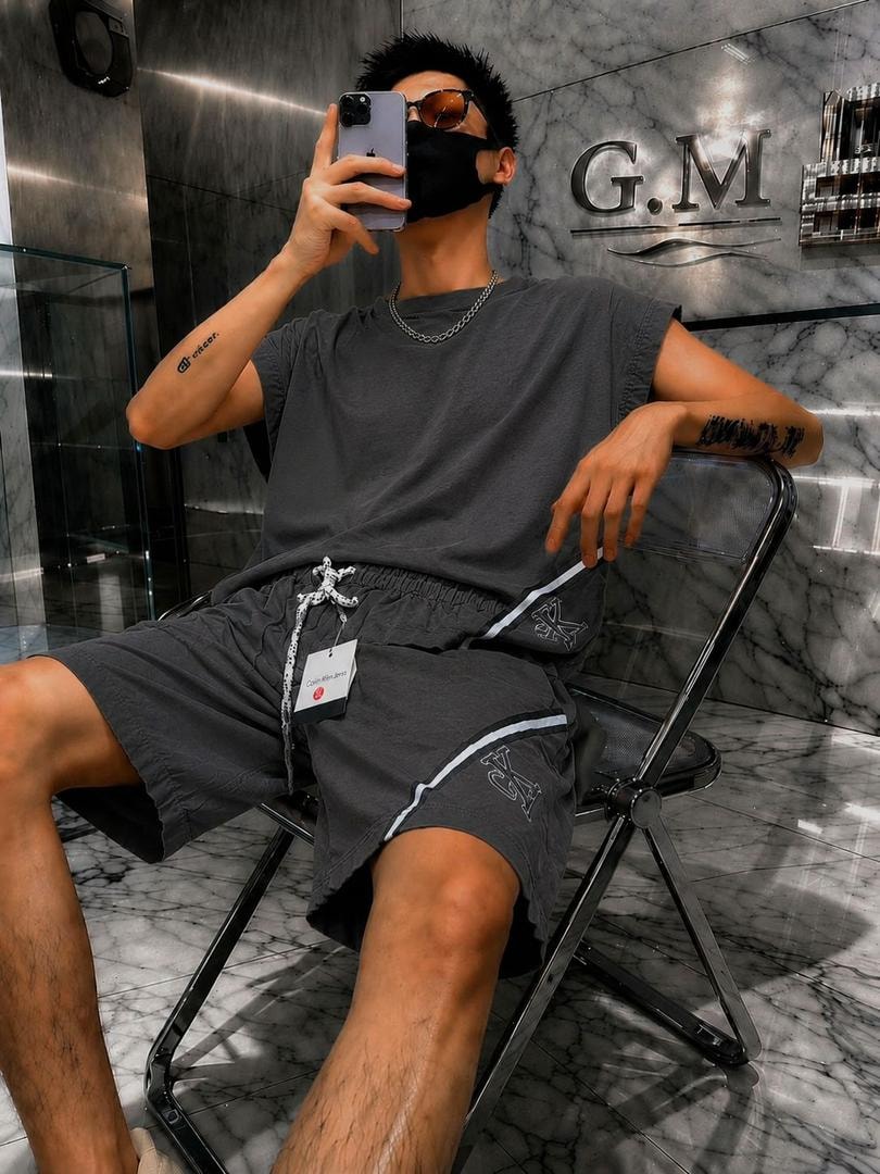 Man in gray short sleeve top and logo shorts with Calvin Klein tag, posing seated in modern interior.