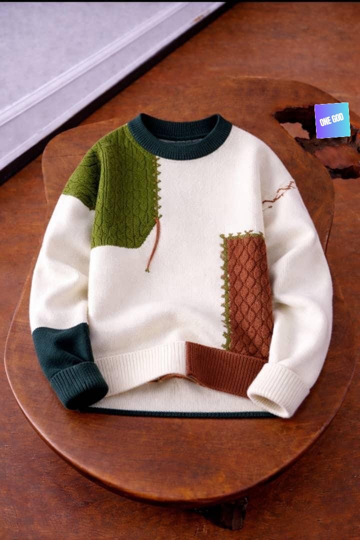 Cream patchwork knit sweater with green and brown panels displayed on wooden stool.
