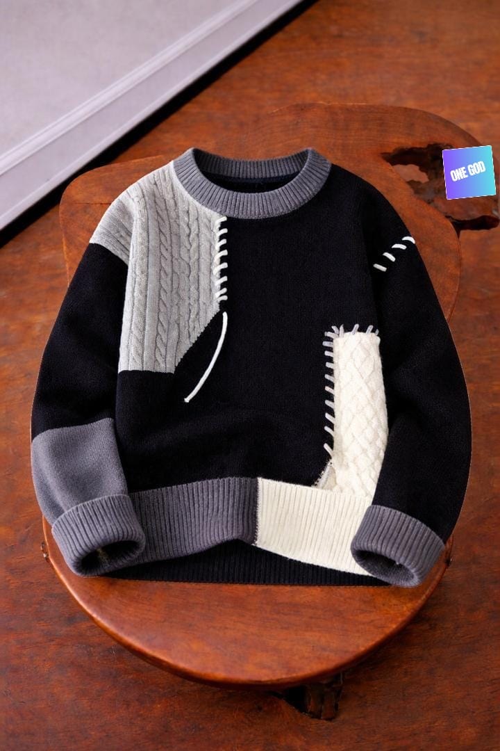 Black patchwork knit sweater with gray and white panels displayed on wooden stool.