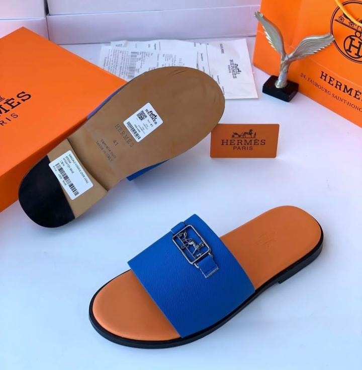 Hermes blue and orange slide sandal with H buckle shown with sole detail and luxury packaging.