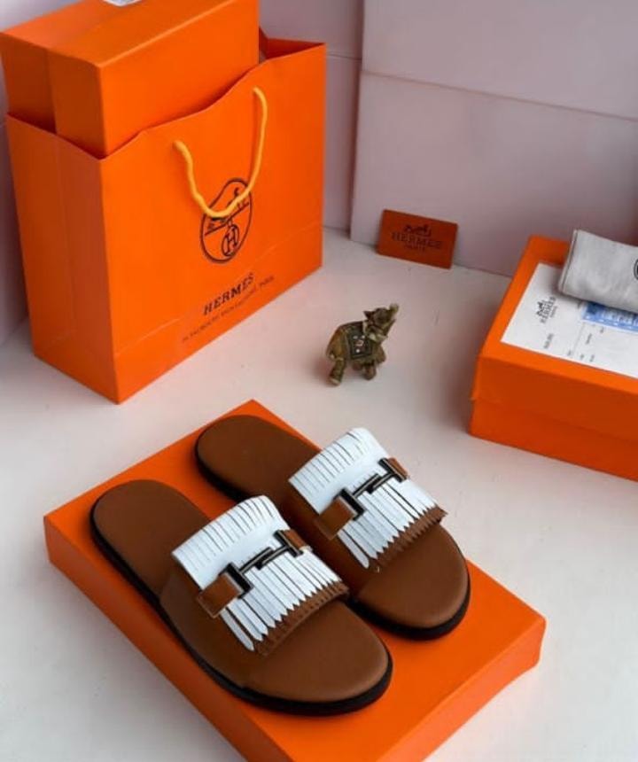 Hermes brown slide sandals with white fringe and H buckle on orange box with shopping bag.