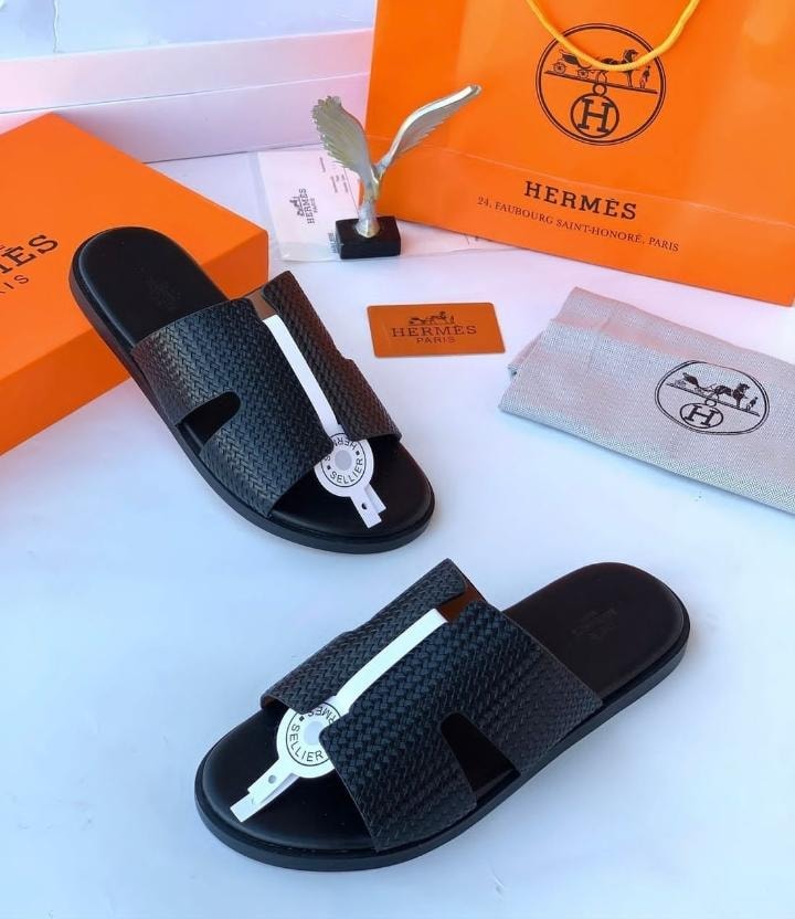 Hermes black woven slide sandals with white accent and luxury packaging including orange boxes and dust bag.