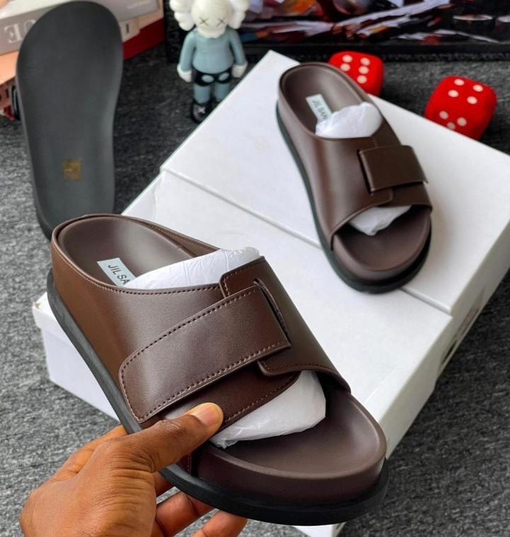 Brown Jil Sander slide held in hand showing the insole label and strap detail.