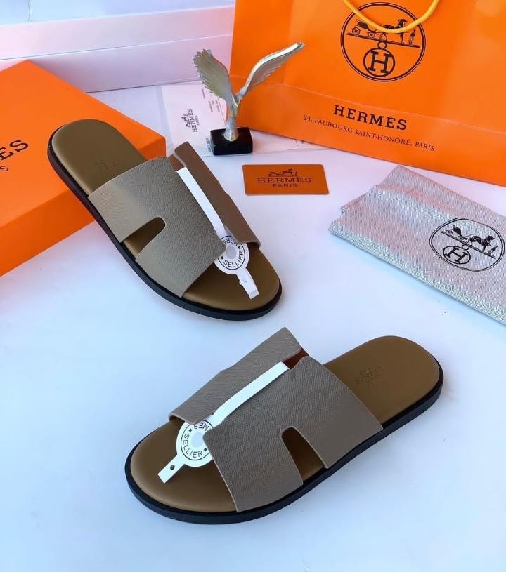 Tan Hermes sandals with white accent strap displayed with orange shopping bag and dust bag.