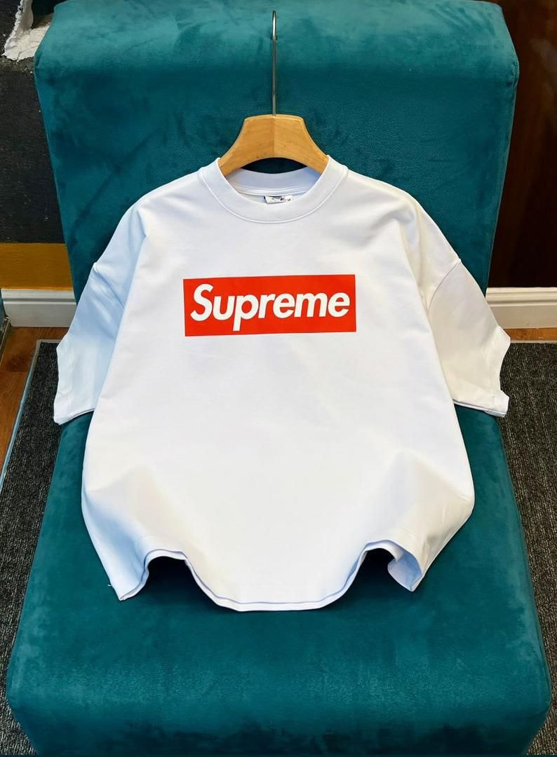 White Supreme box logo crop top on wooden hanger against textured wall.