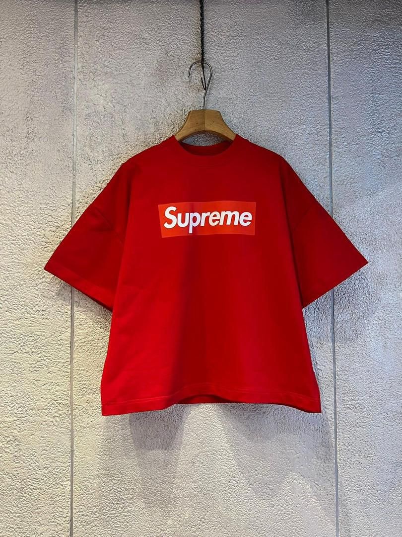 Red Supreme box logo crop top on wooden hanger against textured wall.