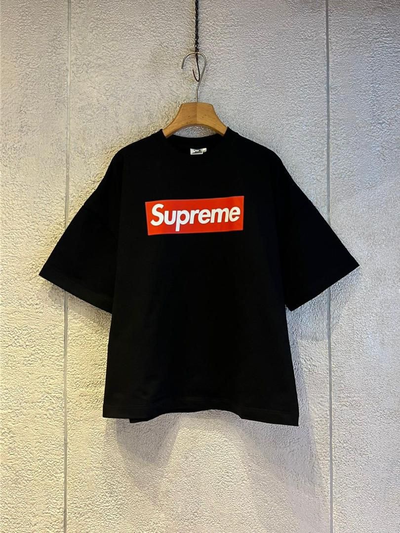 Black Supreme box logo crop top on wooden hanger against textured wall.