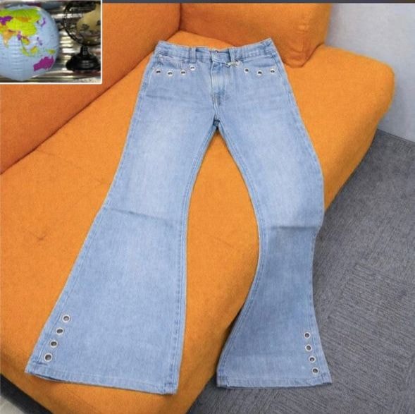Light blue flared jeans with silver eyelets on hems displayed on orange couch.