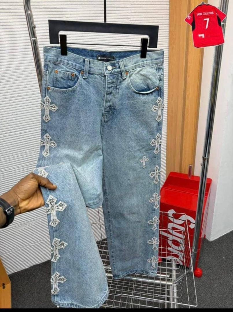 Light blue jeans with silver cross embroidery on legs held for display.