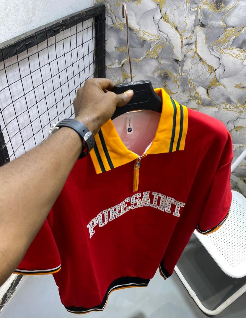 Red short-sleeve polo shirt with yellow collar, green stripes and PURESAINT graphic on chest.