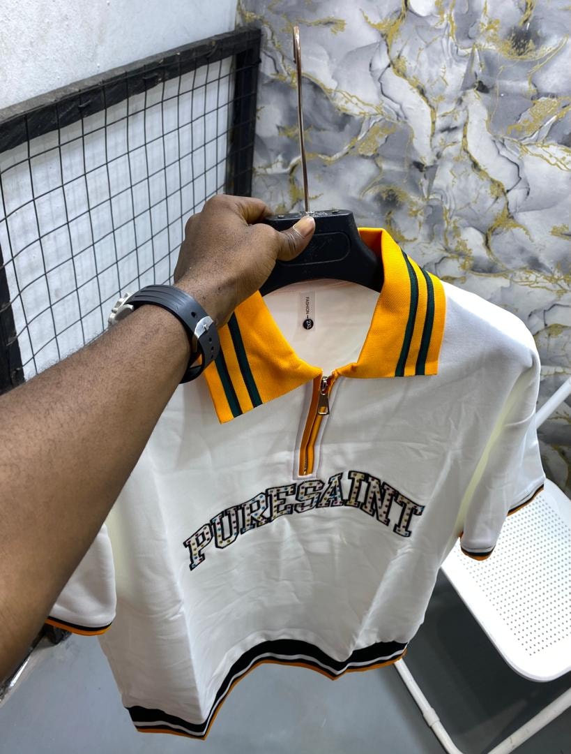 White short-sleeve polo shirt with yellow collar, green stripes and PURESAINT graphic on chest.