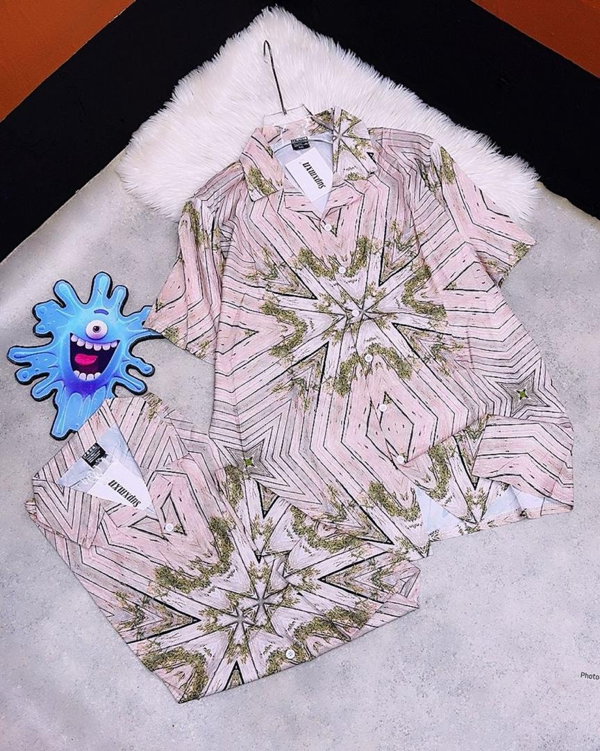 Pink short sleeve shirt with black and green geometric star pattern, shown on hanger and flat.